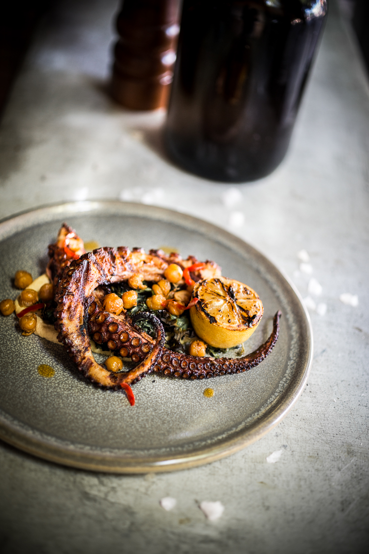 Grilled octopus served with grilled lemon and chickpeas on small grey plate