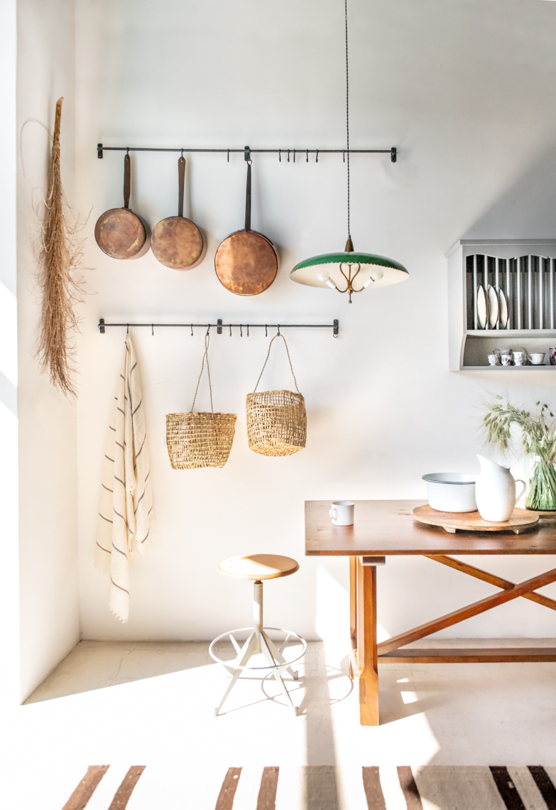 morning light in a kitchen with wooden stool, hanging copper pots, and green antique lamp