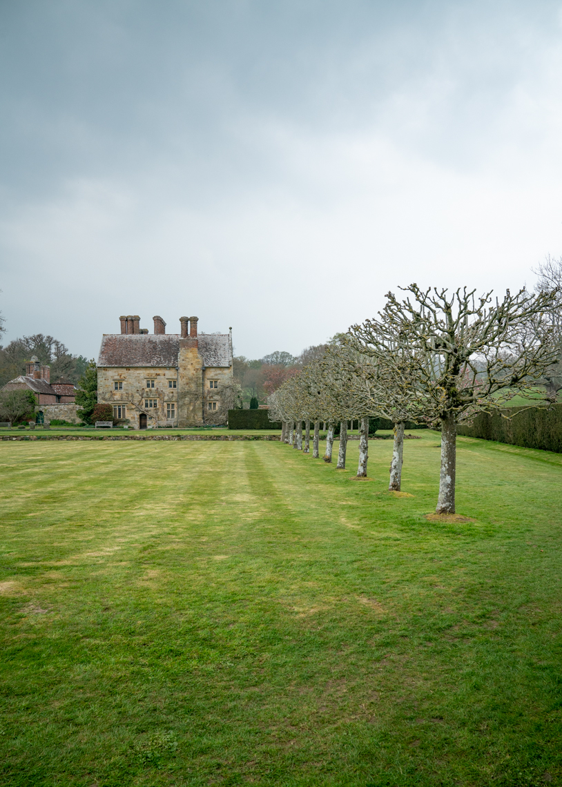 Lawn with lined trees leading to an old english stone house on a spring day