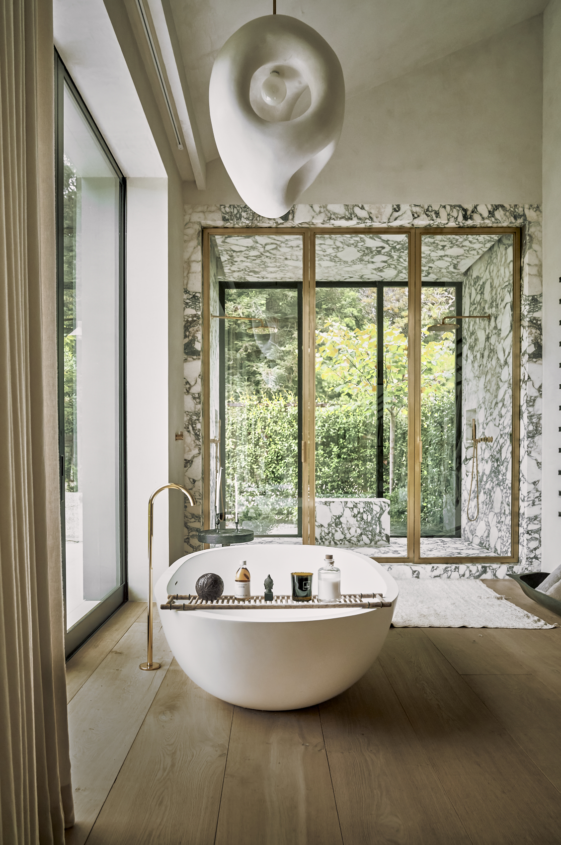 Freestanding white bathtub and large marble shower under shell pendant light