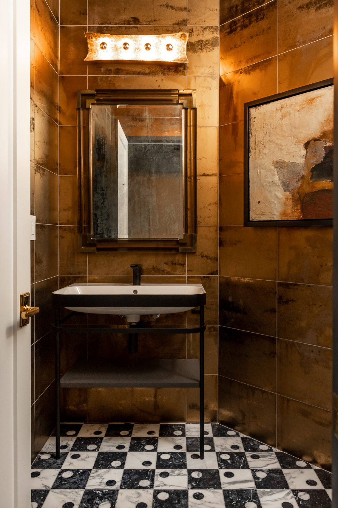 Standing bathroom sink with mirror on checkered floors in small copper walled bathroom.