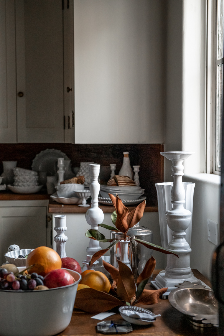 Kitchen table overflowing with porcelain white candle holders and fruit bowl