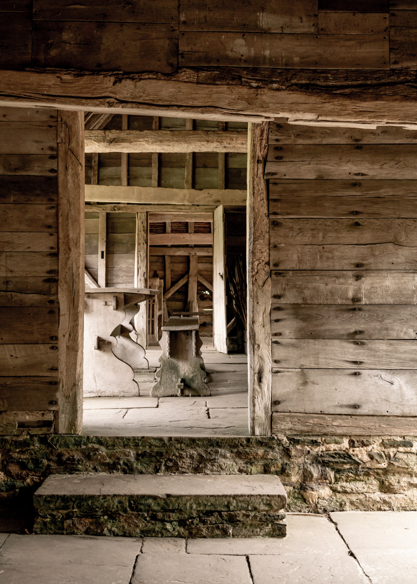 Glimpse into wooden barn with stone accents, stone bench, and table.