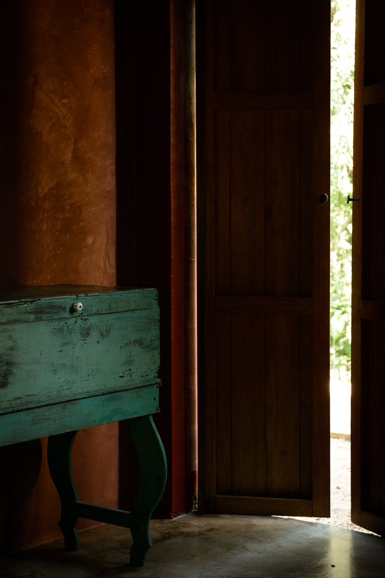 Bright green antique dresser next to cracked open door in dark room in Mexico