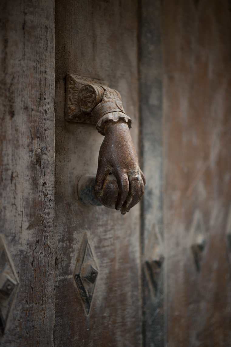 Metal hand-shaped door knocker on old wooden brown door